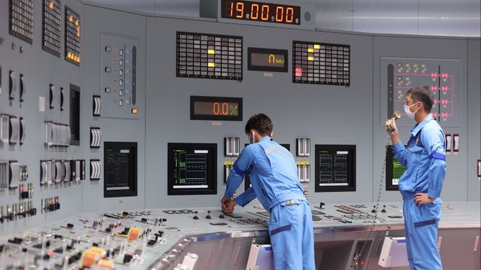 Men in blue uniforms operate a control room filled with monitors, switches and digital displays
