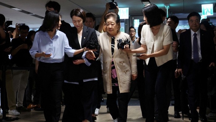 Han Hak-ja walks surrounded by aides and reporters holding microphones as she arrives for questioning at the special prosecutors' office.