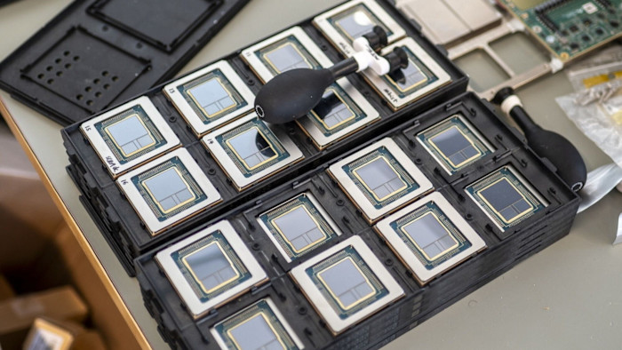 A row of AI chips in protective trays, with two black air blowers resting on top.