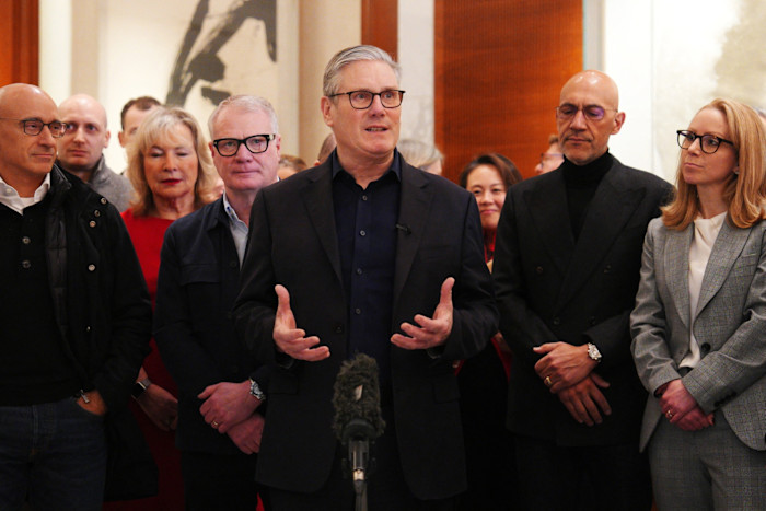 Keir Starmer speaks to a business delegation, gesturing with his hands, as several people stand attentively behind him.