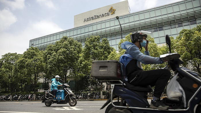 Two delivery workers on motorcycles ride past the AstraZeneca research and development facility in Shanghai.