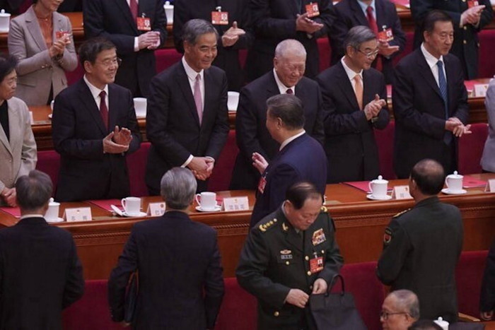 Other senior officials face towards Xi, most of them applauding, as the president passes a uniformed Zhang Youxia, who faces the other way and appears to be fiddling with his bag.