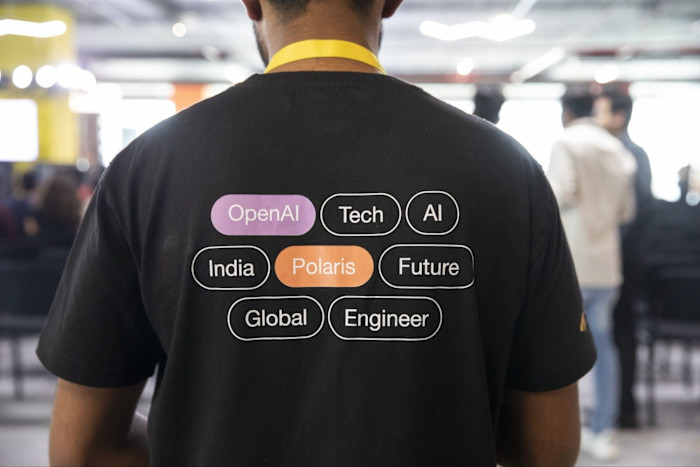 A person wearing a yellow lanyard and a black T-shirt with "OpenAI," "Tech," "AI," "India," "Polaris," "Future," "Global," and “Engineer” printed on the back.