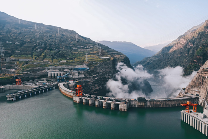 Aerial view of the Baihetan hydropower station dam surrounded by mountains and mist, with green water in the reservoir.