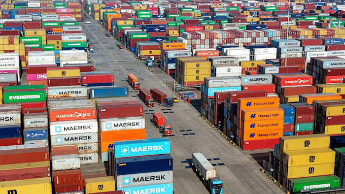 Rows of shipping containers in various colors stacked high at Qingdao Port, with trucks moving along lanes between the stacks.