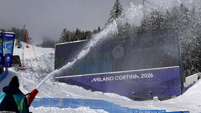 A staff member sprays artificial snow near signage for Milano Cortina 2026 at the Tofane Alpine Skiing Centre.