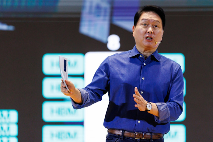 Chey Tae Won speaks on stage holding papers, gesturing with one hand, at the SK AI Summit.