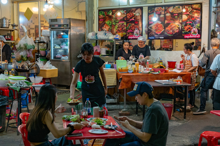A waitress hands a dish of food to a couple at a restaurant on Banthat Thong street