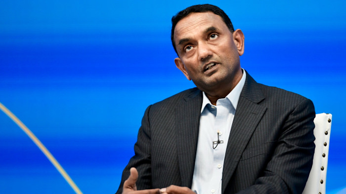 K. Krithivasan speaks while gesturing with his hands during a press conference, seated against a blue background.