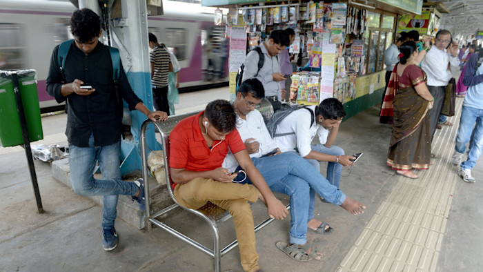 Several people use their phones at a free Wi-Fi zone inside a busy suburban railway station in Mumbai