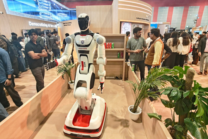 A humanoid Jio robot labeled "ADDVERB" is displayed at a convention booth, surrounded by attendees at the India AI Impact Summit.