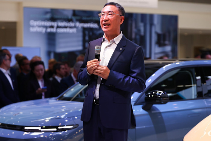 Zhu Jiangming speaks into a microphone in front of a blue car at the IAA Mobility 2025 expo in Munich.