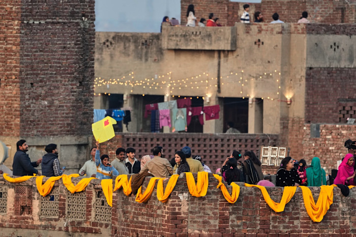 Mixed groups of men and women gather on rooftops decorated with strings of lights and decorative drapery of bold yellow fabric.