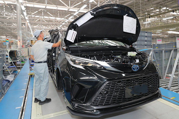 An employee works on the assembly line beside a black Toyota new energy vehicle with its hood open at a FAW Toyota plant.