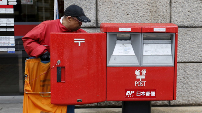 A Japan Post Co worker in a red jacket collects mail from a large red post box outside a post office in Tokyo.