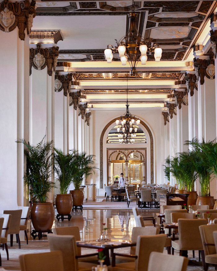 The Peninsula’s elegant lobby with high ceilings, chandeliers, ornate columns, potted plants and tables set for dining.