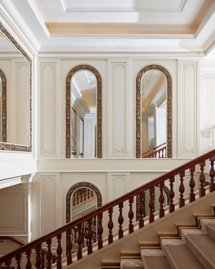 Grand staircase with ornate wooden banister and arched mirrors in an elegant, cream-coloured lobby at The Peninsula Hong Kong.