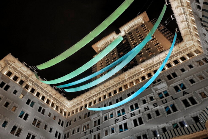 ‘Esmeralda’ by Kingsley Ng — one of the installations at The Peninsula during its 2024 Art in Resonance programme: long, illuminated fabric ribbons in blue and green shades suspended above the hotel’s courtyard, seen here at night.
