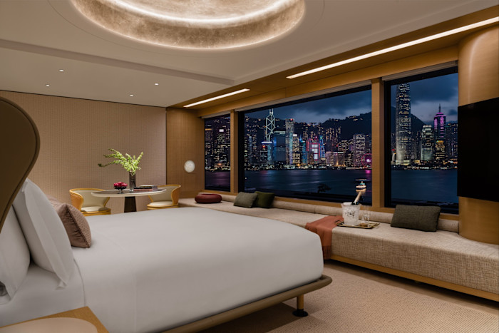 The Regent Hong Kong’s Harbourview Suite, with a large bed, a sitting area and floor-to-ceiling windows displaying a night view of Hong Kong’s skyline and Victoria Harbour.