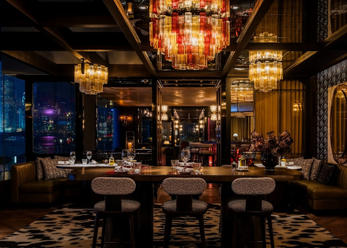 The hotel’s Qura Bar, with dim lighting, plush seating, set dining tables, and large coloured chandeliers, overlooking city lights.