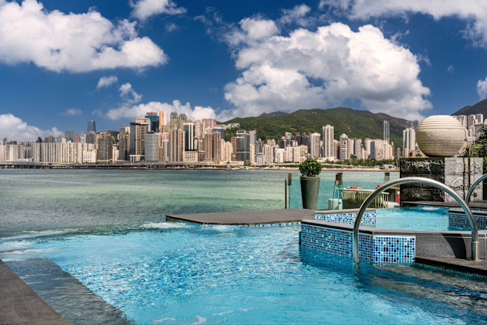 Infinity pool at Regent Hong Kong overlooking Victoria Harbour with Hong Kong skyline and mountains in the background.