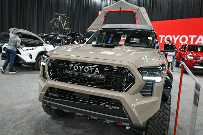 A 2025 Toyota Tacoma Hybrid pickup truck on display at the Edmonton Motor Show, with other Toyota vehicles in the background.