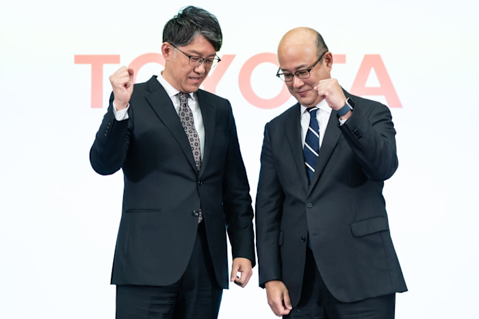 Koji Sato and Kenta Kon stand together, both raising clenched fists, in front of a Toyota logo.