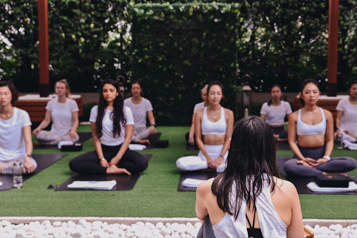 A group of people practise yoga outdoors on mats, seated in meditation poses, with a yoga instructor facing them at Upper House Hong Kong.
