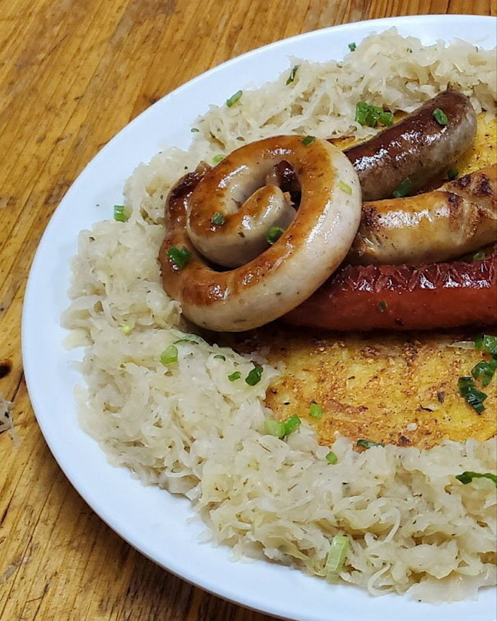 A plate with assorted grilled bratwurst sausages, sauerkraut and a golden potato pancake, garnished with chopped green herbs at The Hong Kong Outpost.