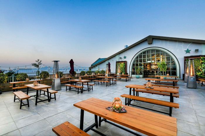 Outdoor dining area at Pier 7 in Hong Kong with wooden picnic tables, string lights and patio heaters, overlooking the water.