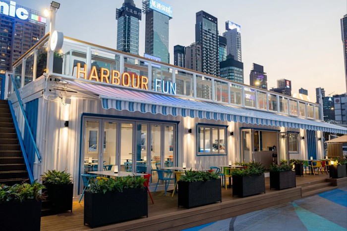 The Harbour Fun venue in Hong Kong: a modern, two-level building with outdoor seating, colourful chairs and city skyscrapers in the background.