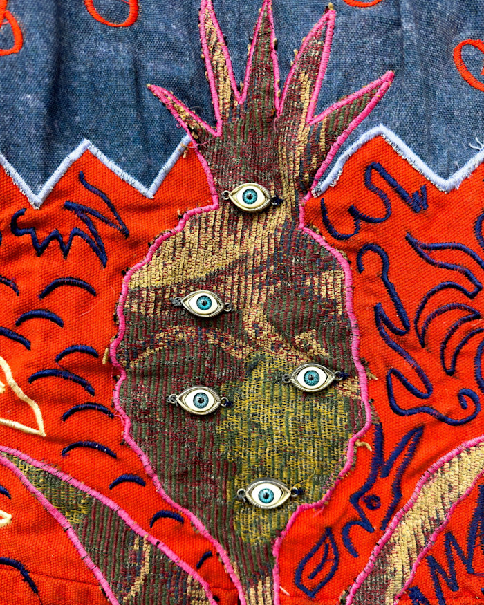 A detail from Cian Dayrit’s tapestry, pictured on the left, showing metal eye badges superimposed on the shape of a pineapple