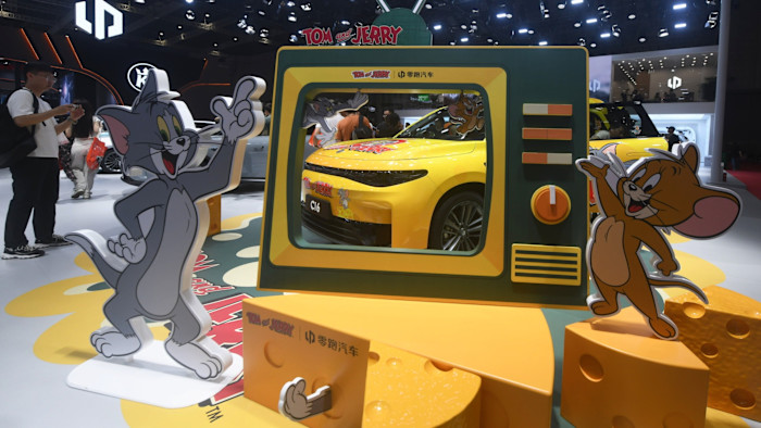 A yellow Leapmotor car with Tom and Jerry branding is displayed behind cartoon cutouts of Tom and Jerry at the Shanghai Auto Show.
