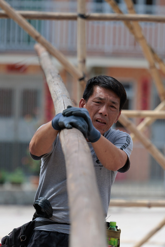 Veteran scaffolder Lai Chi-ming carries a long bamboo pole on his shoulder while working in a temporary bamboo theatre.