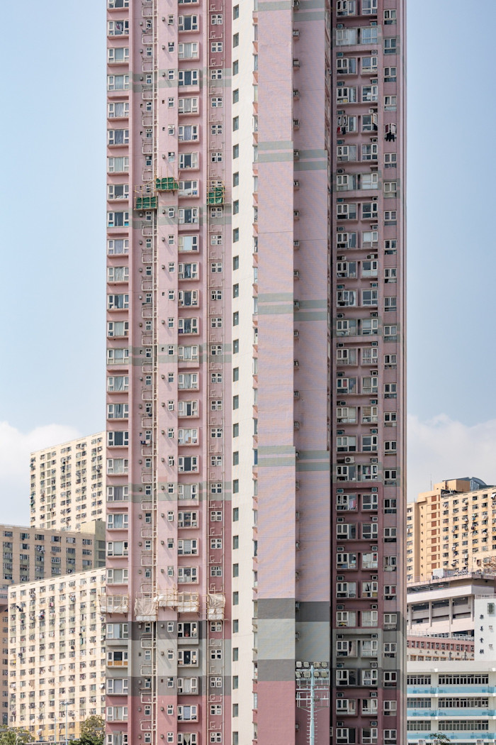 Scaffolding platforms made of bamboo and aluminium are attached to the upper and lower sections of a tall pink residential building.