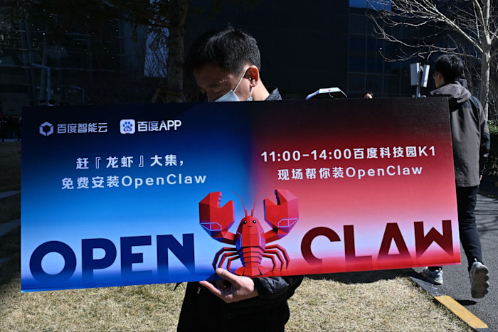 A man wearing a face mask holds a placard promoting OpenClaw, an open-source AI assistant, with a large illustrated lobster and bilingual text.
