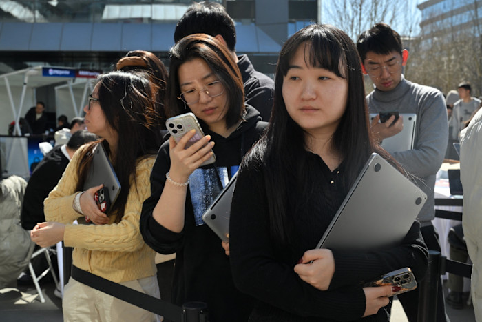 People stand in line holding laptops and phones, waiting outdoors at Baidu headquarters.