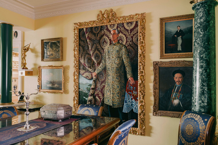 A view of Chris Hall’s dining room, featuring a large ornate portrait of him in traditional attire, surrounded by antique decorative objects and other paintings from Europe and the Far East.
