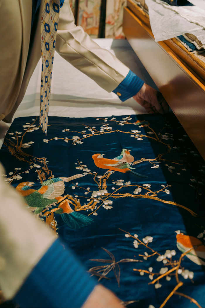 Chris Hall arranges a dark blue textile embroidered with colourful birds and blossom branches.