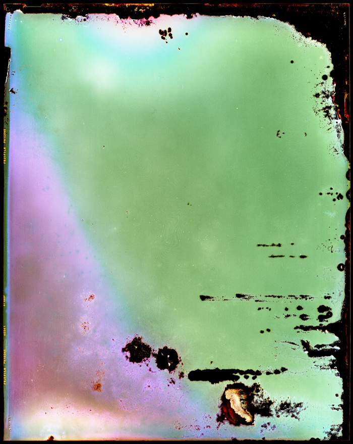 A luminous green and purple surface is dotted with dark blotches, spidery fissures and patterns of concentric circles, alternately dark and bright. The image was created by leaving large-format silver halide film in radioactive soil for six months and then developing it