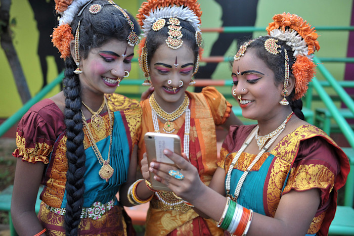 Indian girls, dressed for a traditional dance performance, looking at a mobile phone