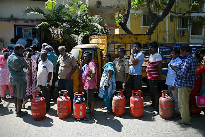People stand in a long queue beside multiple red LPG cylinders outside a gas agency office in Chennai.