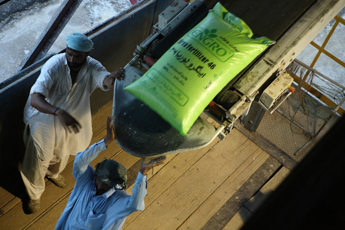 Two Engro Fertilizers Ltd. employees handle a large green sack of urea fertiliser on a conveyor belt at the company’s plant