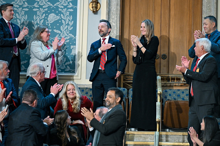 Brad Gerstner stands with his hand over his heart as people around him applaud during the State of the Union address.