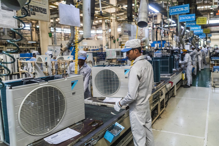 Workers in uniforms assemble outdoor units of split system air conditioners on a factory assembly line at Daikin Air Conditioning India.