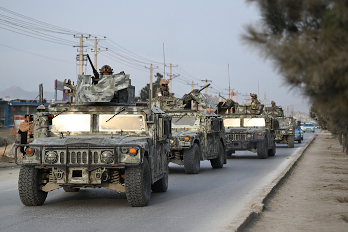 Taliban security personnel in camouflage uniforms ride in armored Humvees along a city street in Kabul.