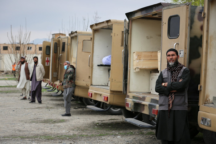 Several men stand near a row of ambulances with open doors, some containing coffins, at the site of an air strike in Kabul.
